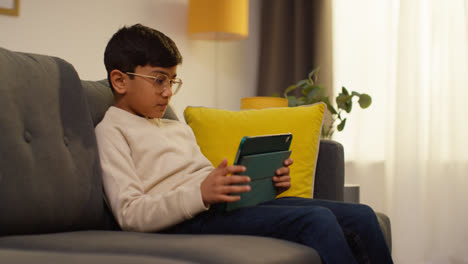 Young-Boy-Goes-To-Sit-On-Sofa-At-Home-And-Play-Games-Or-Stream-Content-Onto-Digital-Tablet